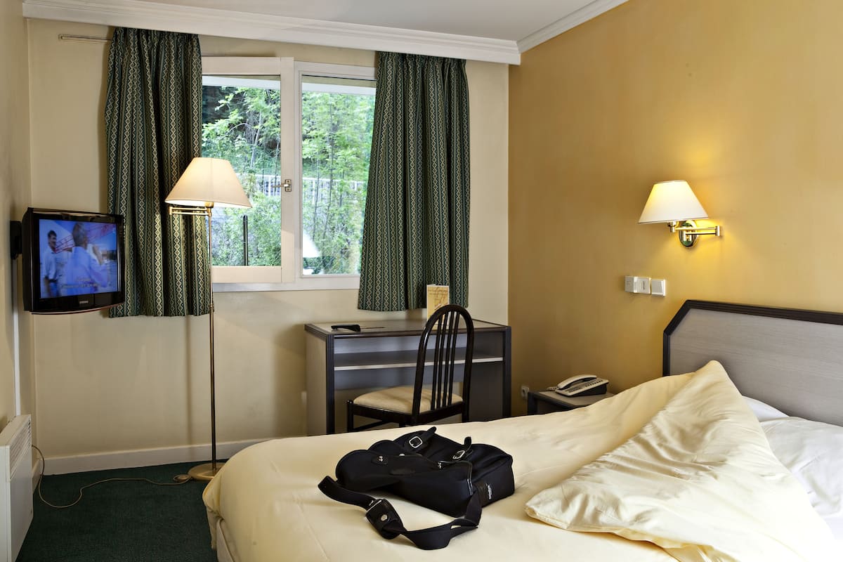 Habitación de hotel con una cama, un escritorio con silla, un televisor y dos lámparas de pared.