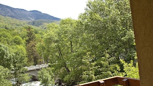 Un balcón con baranda de madera, una silla de madera y vistas a un río y colinas boscosas.