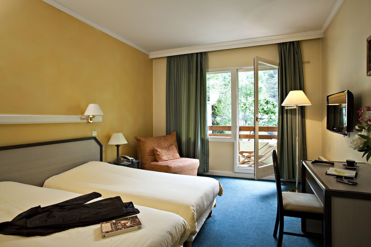 Habitación de hotel con dos camas, un escritorio, una silla, una lámpara y vistas al exterior.