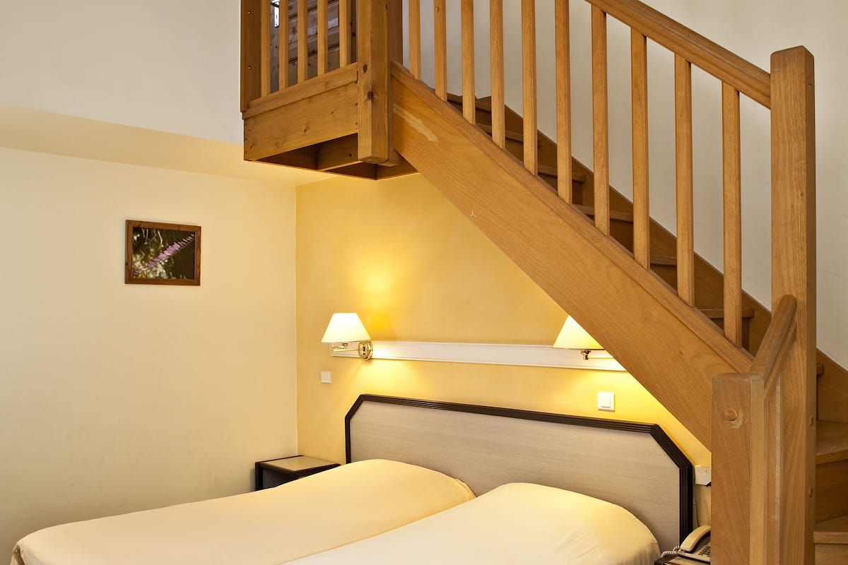 Un dormitorio con dos camas, una escalera de madera, una mesita de noche y una lámpara fijada a la pared.