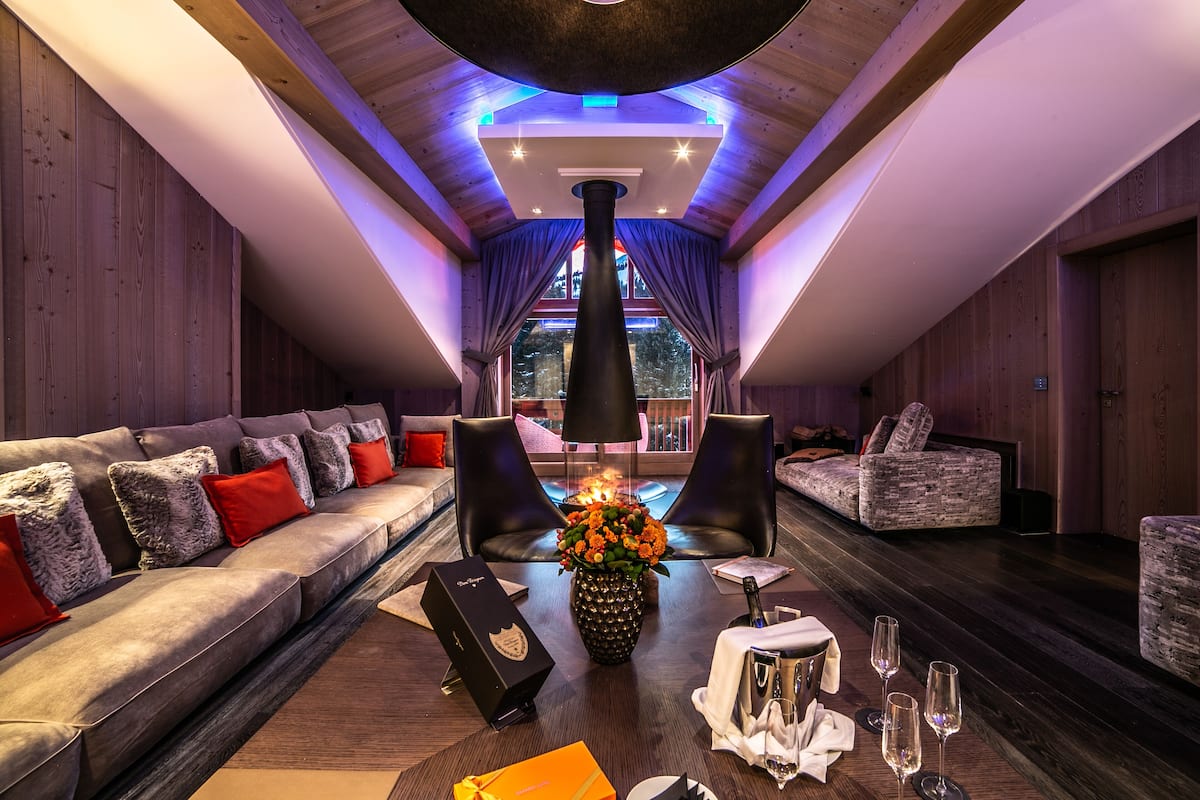 A modern lounge area with a sofa, chairs, a table with a vase of flowers, and a fireplace.