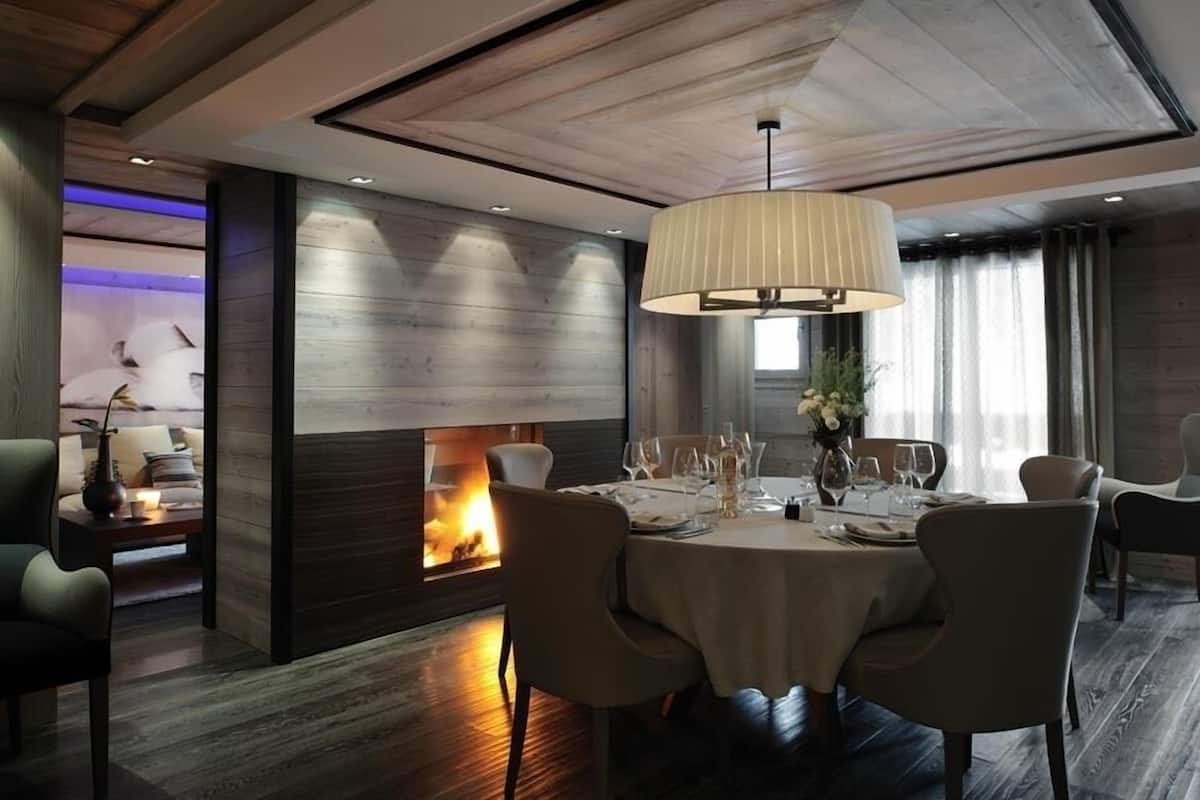 A dining area with a fireplace, a round table set for four, and a modern chandelier.