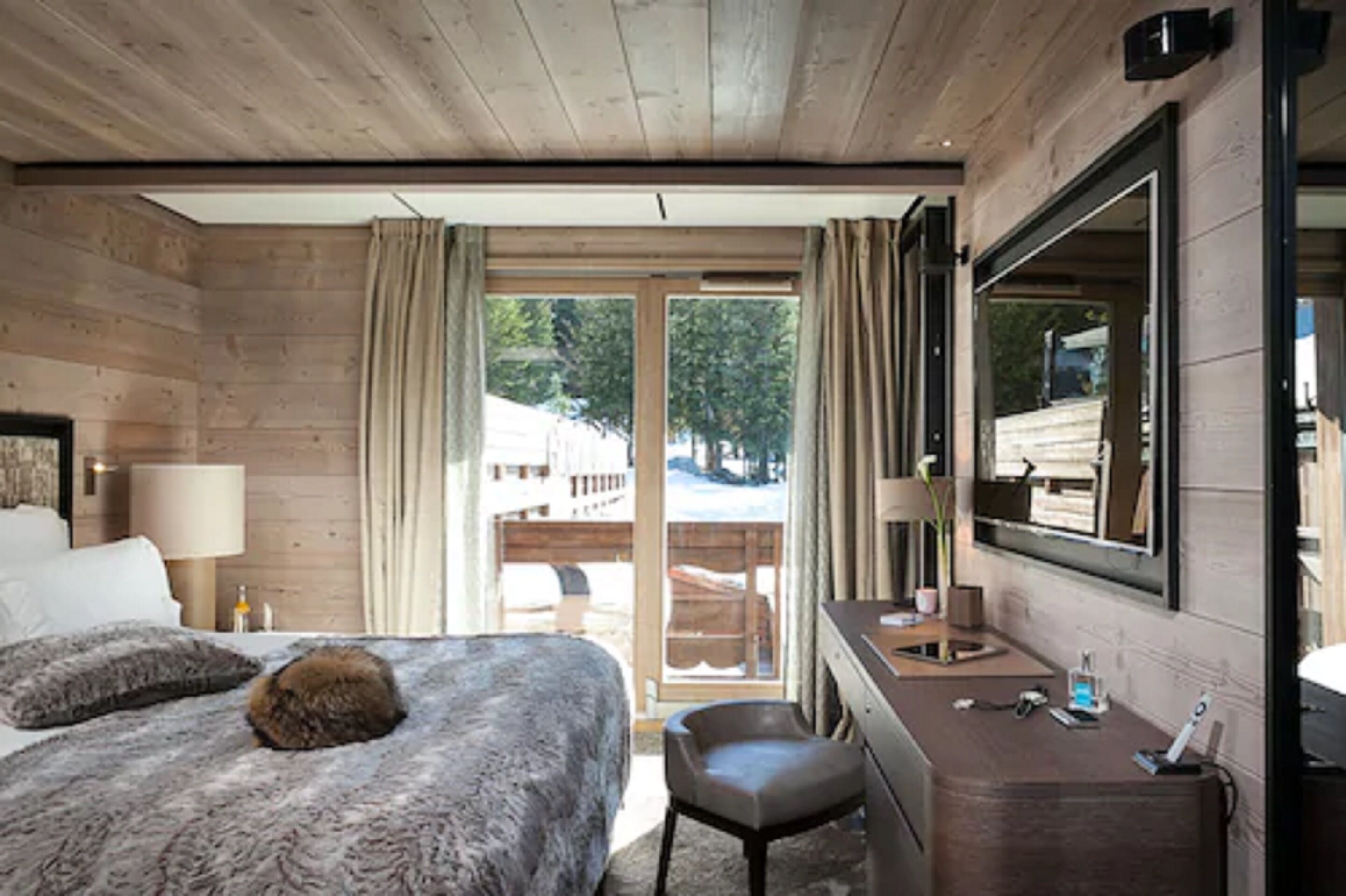 Une chambre d’hôtel avec un intérieur en bois, un lit recouvert d’une couverture moelleuse, un bureau avec un miroir et une vue sur l’extérieur.
