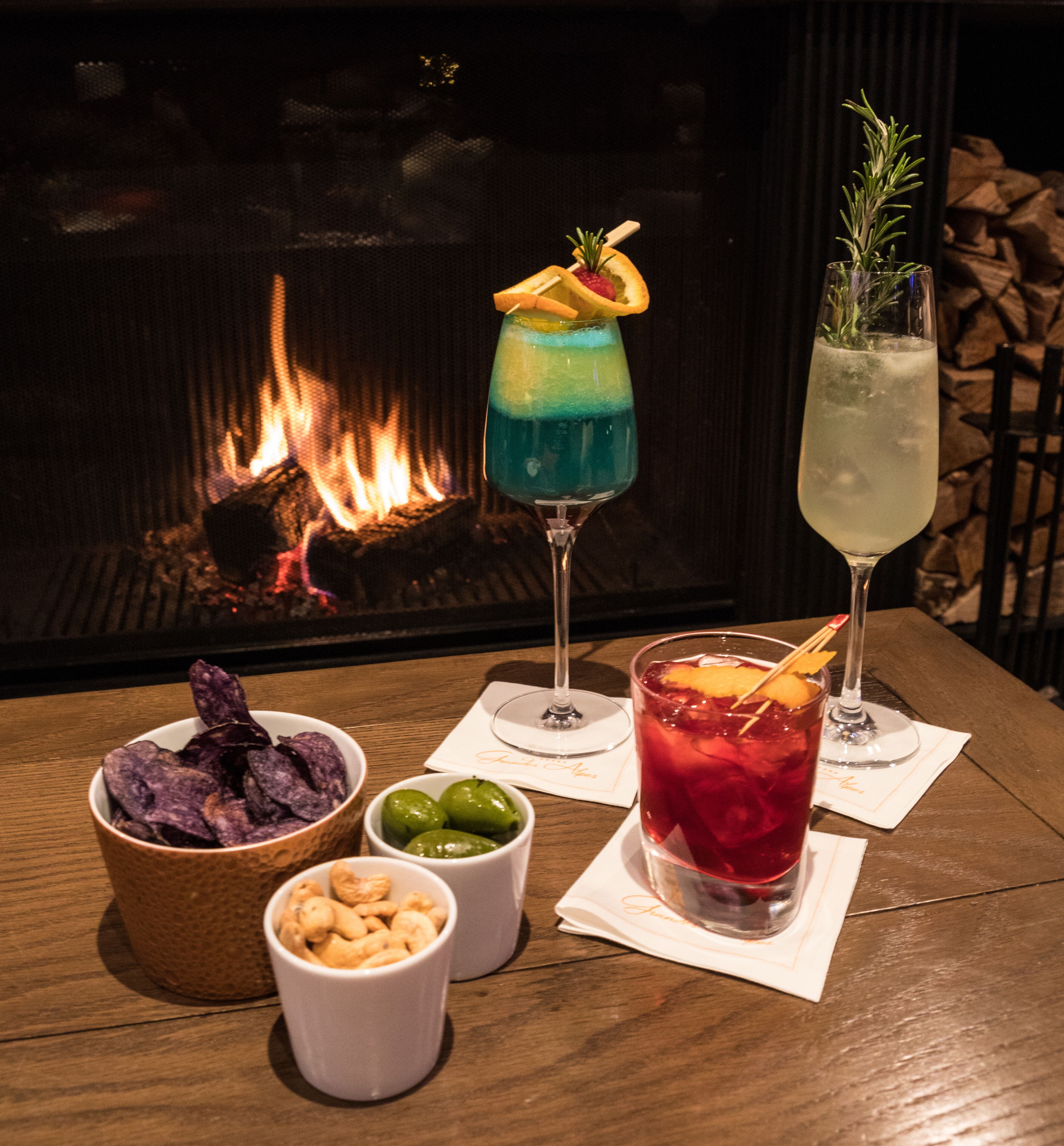 Une table avec trois boissons, un bol de chips et deux petits bols contenant des noix et des olives.