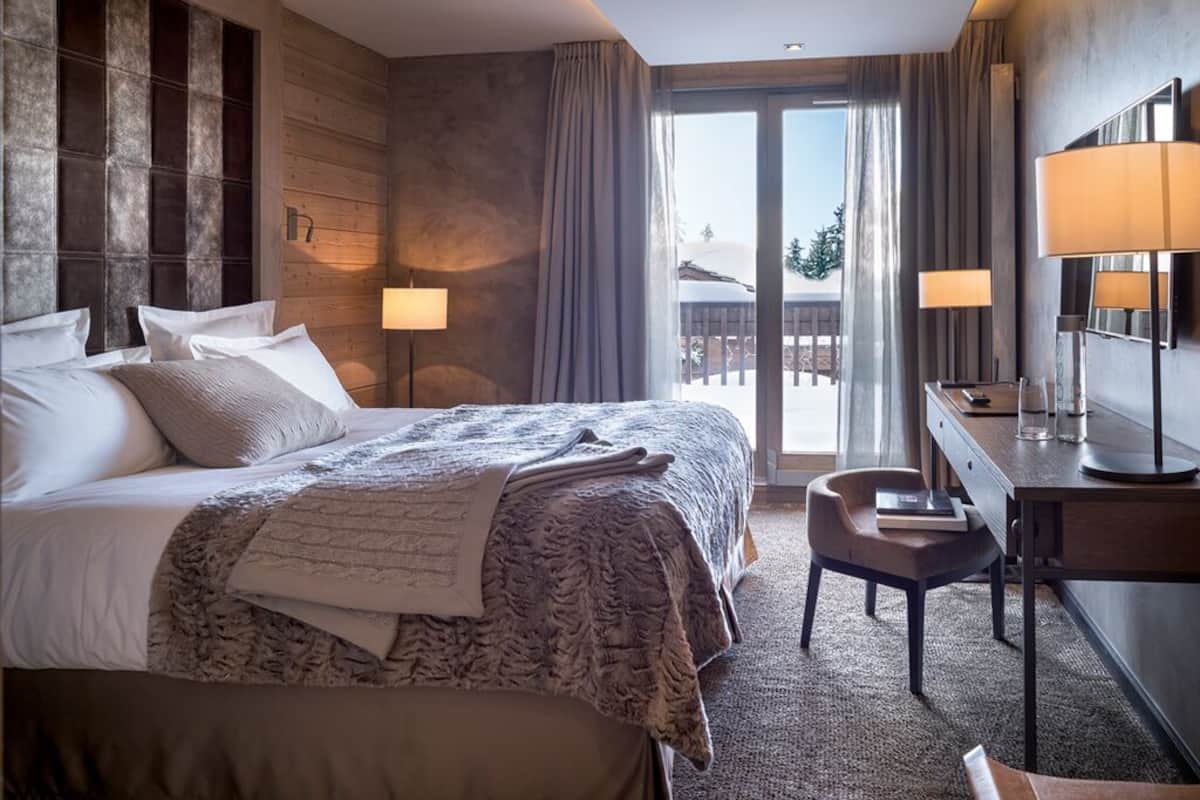 A hotel room with a large bed, a desk, a chair, and a view of the outdoors.