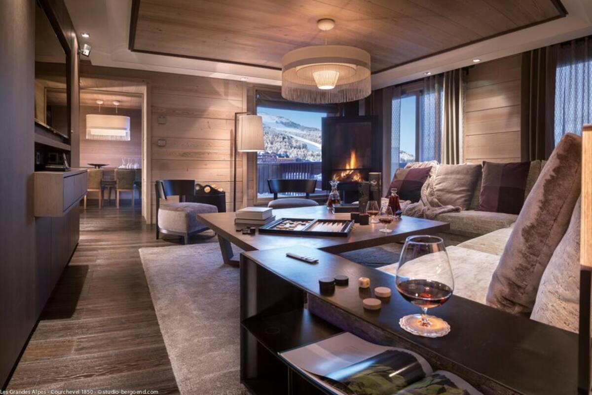 A modern hotel room with a fireplace, a sofa, a dining table, and a view of the mountains.