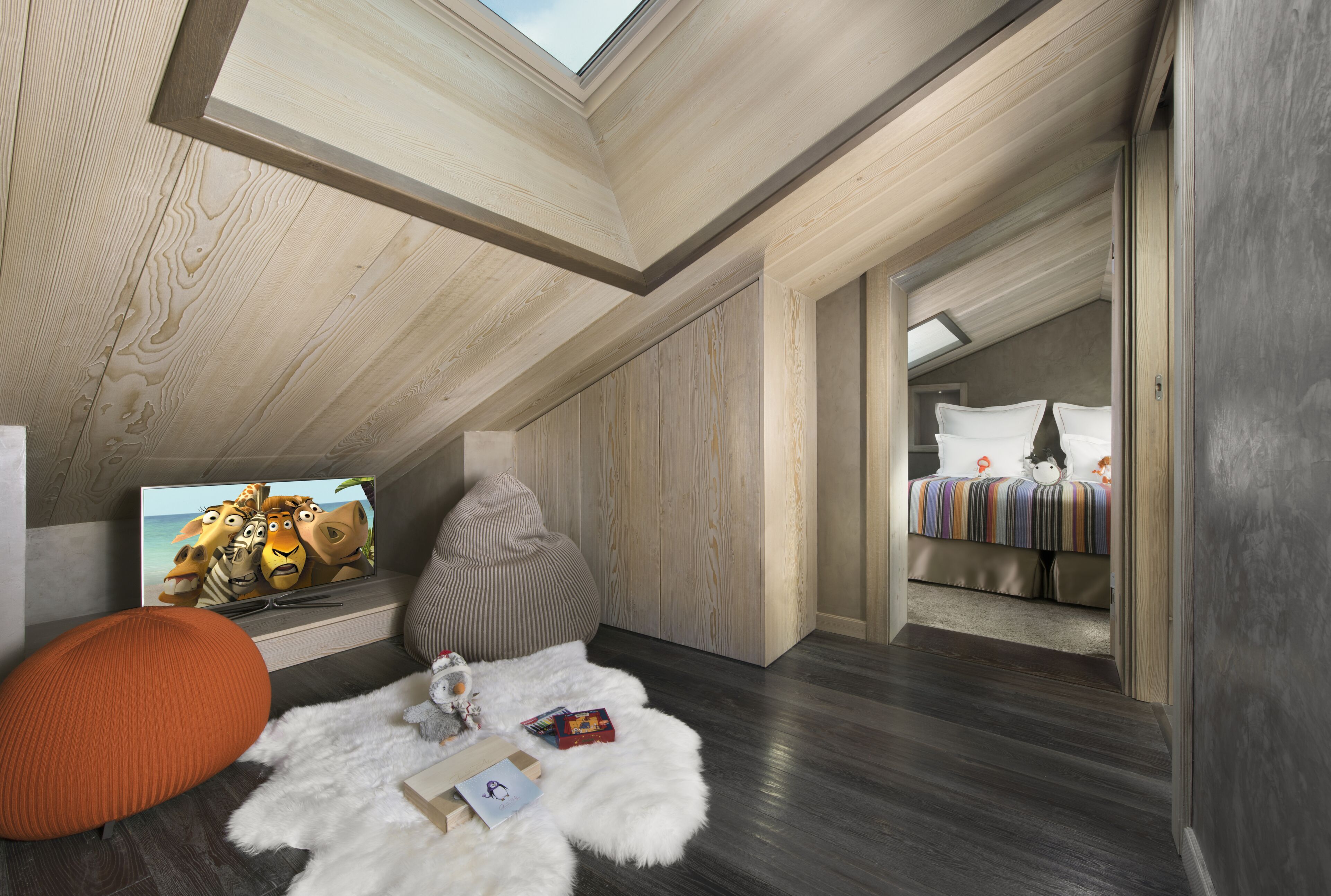 Une chambre de style loft moderne, dotée d’une lucarne, de murs en bois, d’un coin salon confortable et d’un lit recouvert d’une couverture à rayures.