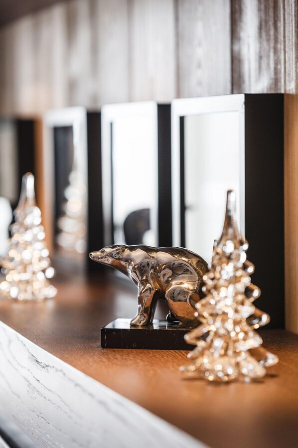 A polished wooden bar counter with a reflective surface, flanked by two glass Christmas trees and a silver animal figurine. - Grandes Alpes Hotel (Courchevel)
