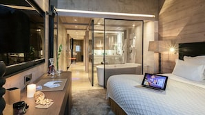 A modern hotel room with a bed, a laptop, a desk with a candle, and a view of the bathroom.