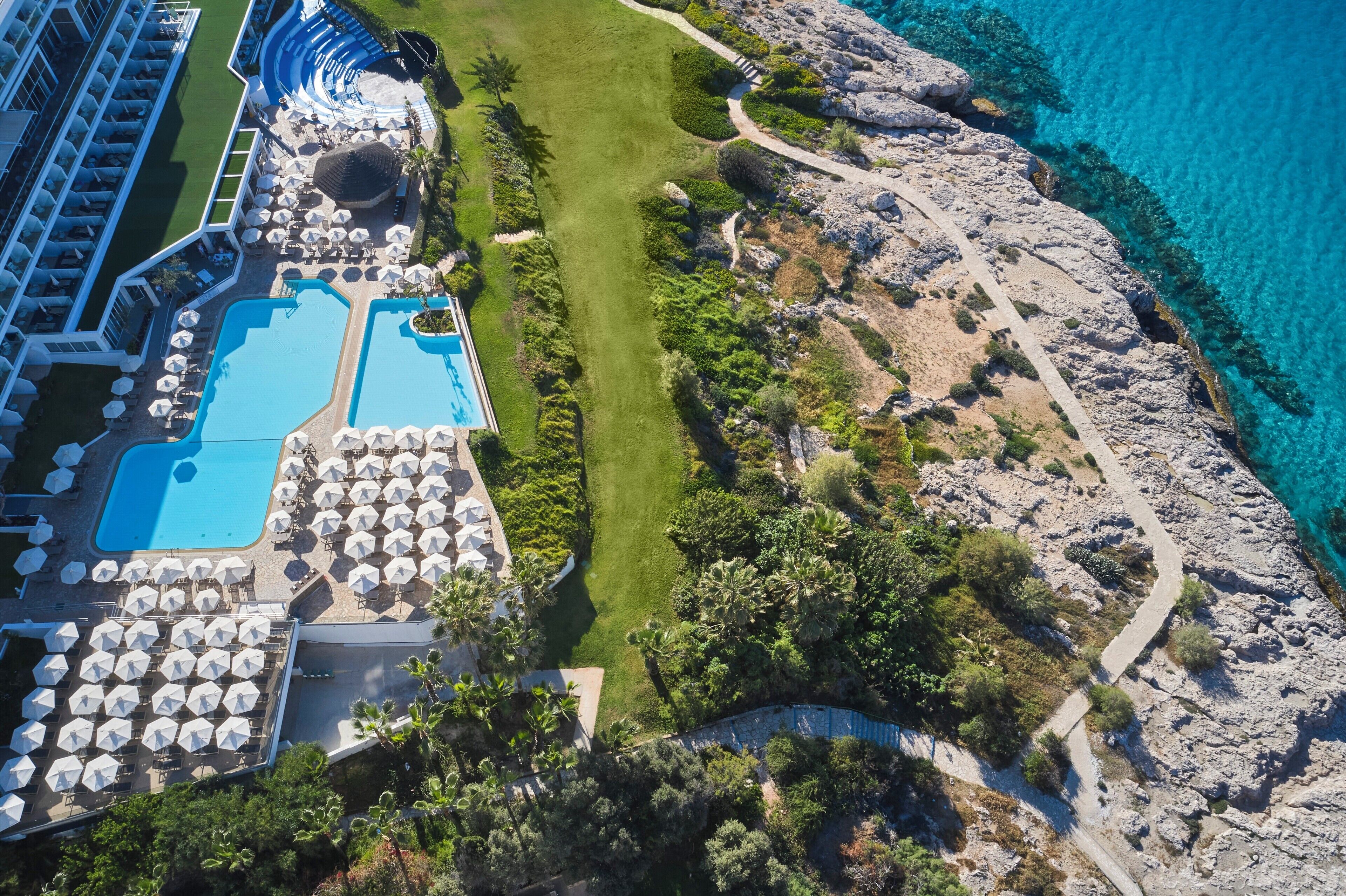 An aerial view of a resort with multiple swimming pools, sun loungers, and a rocky coastline.