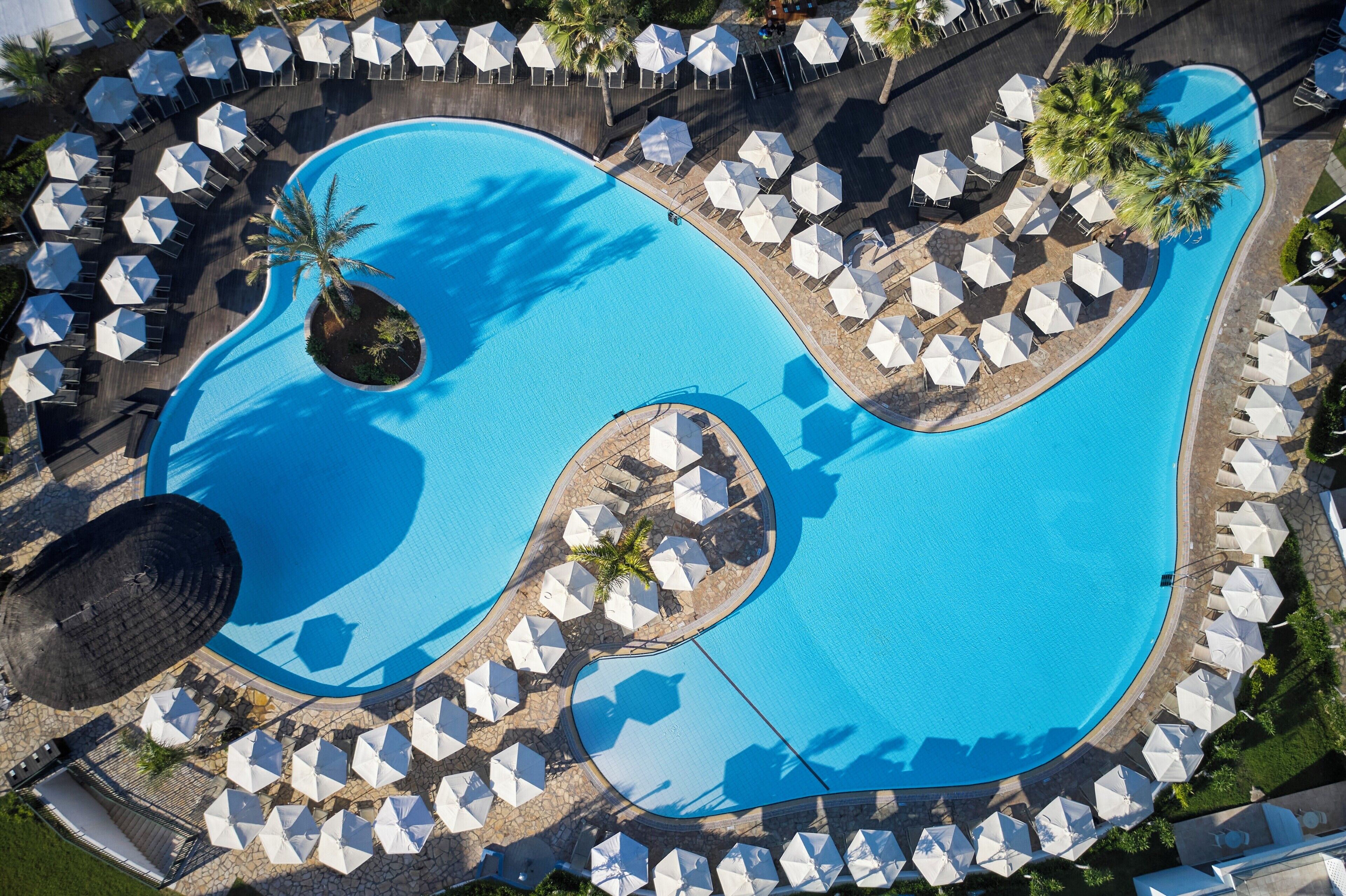 En vy från ovan av ett semesterområde med en stor swimmingpool, solstolar och parasoller.