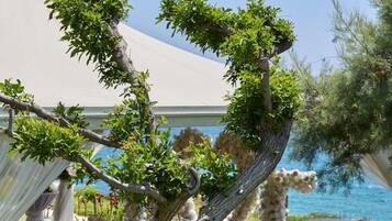 An outdoor wedding venue with a clear view of the sea, arranged tables with chairs, and a decorative archway.