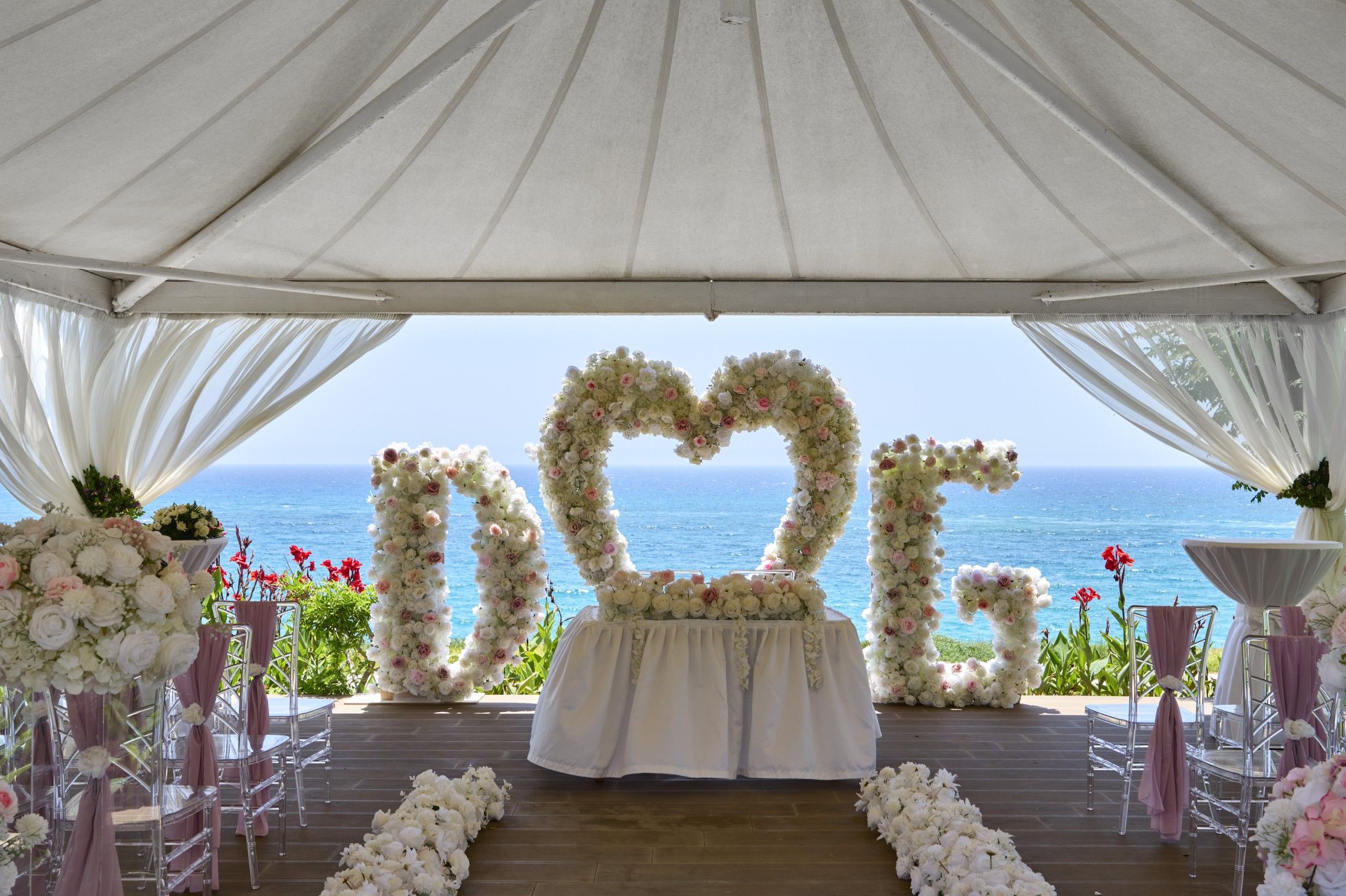 Espaço para casamento ao ar livre, com arco floral em formato de coração e vista para o oceano.