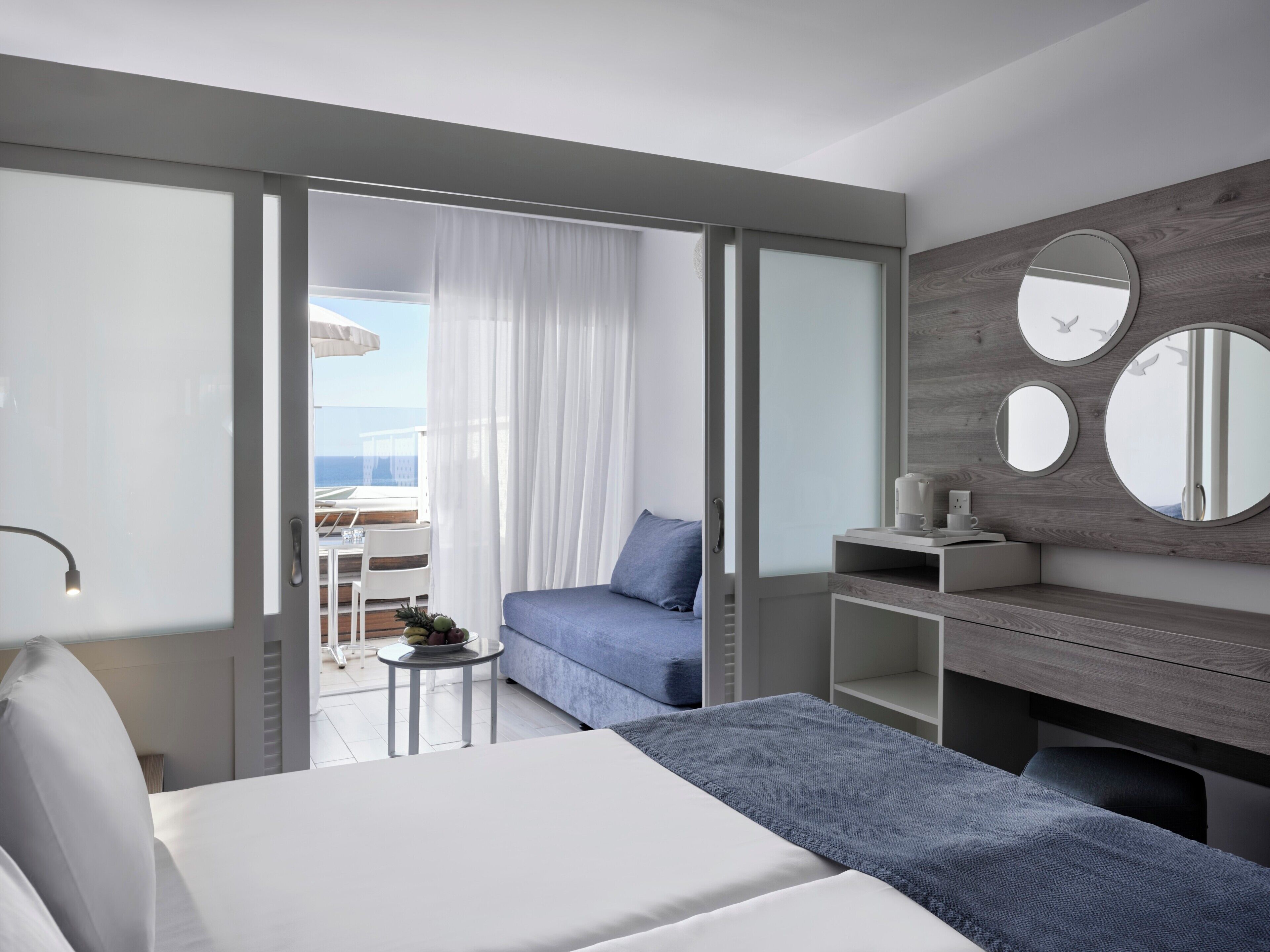 Habitació d'hotel moderna amb llit, escriptori, cadira, taula petita amb una planta i vistes a l'oceà a través d'una porta corredissa.