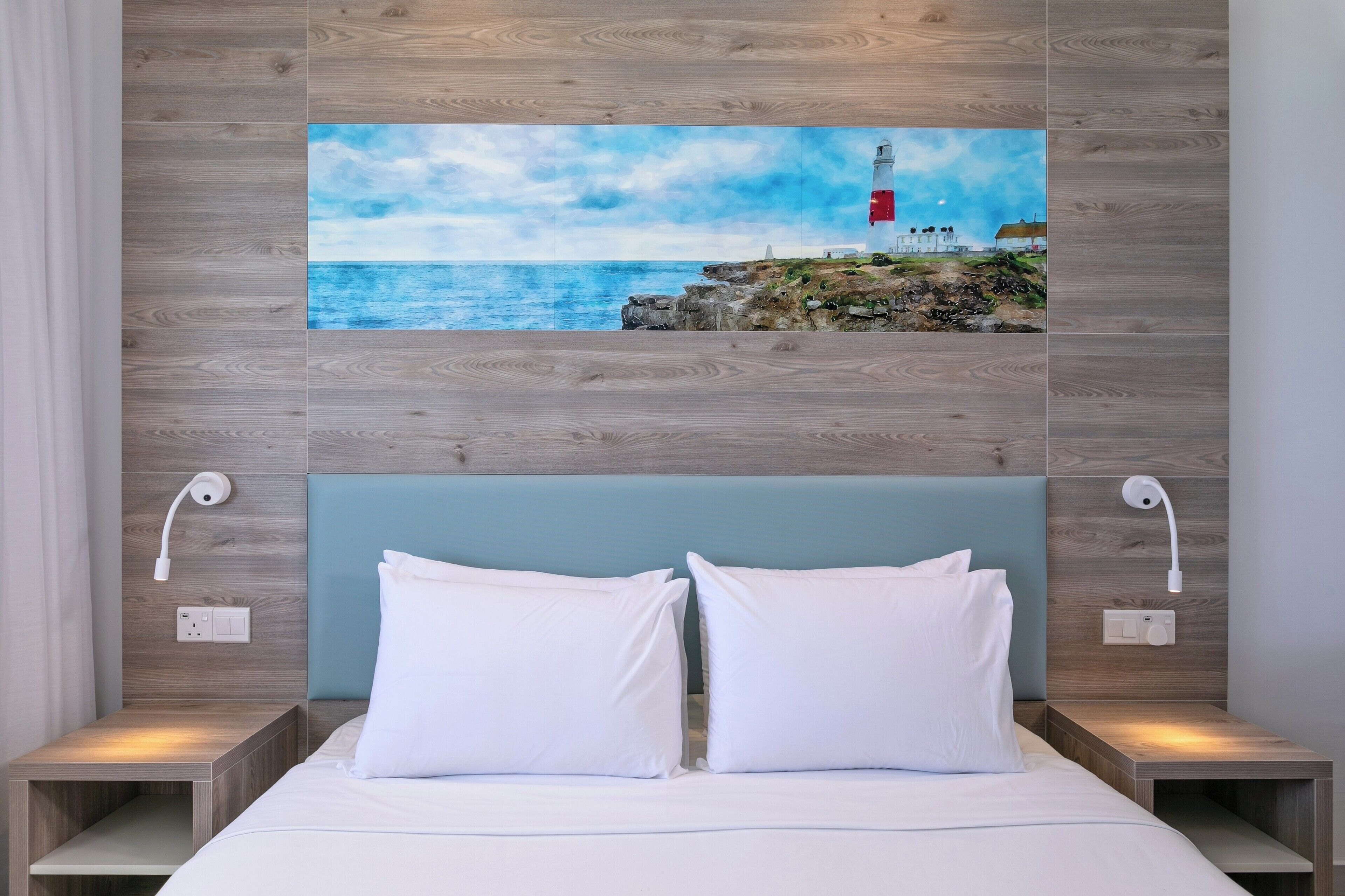 Een slaapkamer met een houten hoofdeinde, witte beddengoed en een schilderij van een vuurtoren aan de muur.