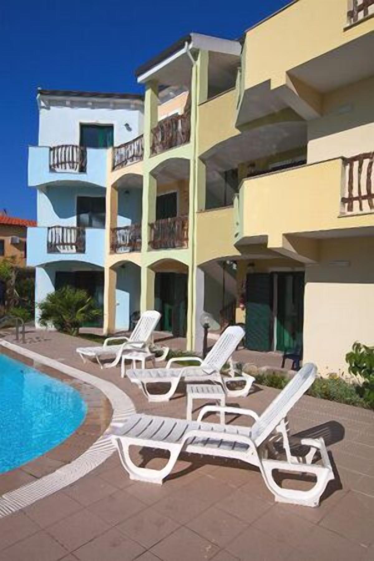 A hotel with multiple balconies, a swimming pool, and lounge chairs.