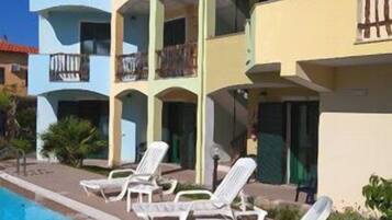 A hotel with multiple balconies, a swimming pool, and lounge chairs.