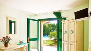 A room with a desk, chair, and a view of a swimming pool outside. - Ariadimari Hotel (Valledoria)