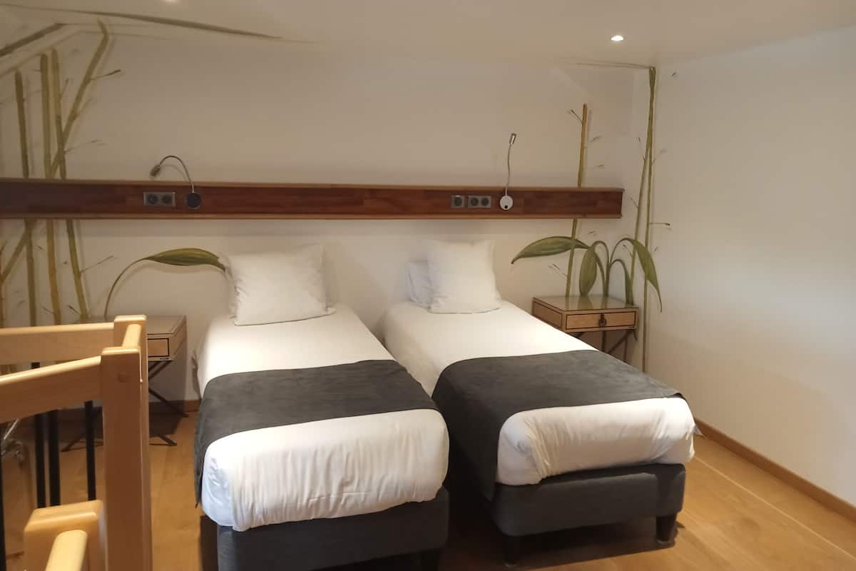A double room with two beds, a wooden headboard, bedside tables, and a plant.