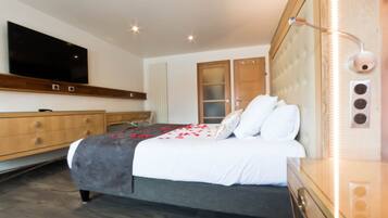 A modern bedroom with a large bed, a TV mounted on the wall, a wooden dresser, and a glass cabinet.