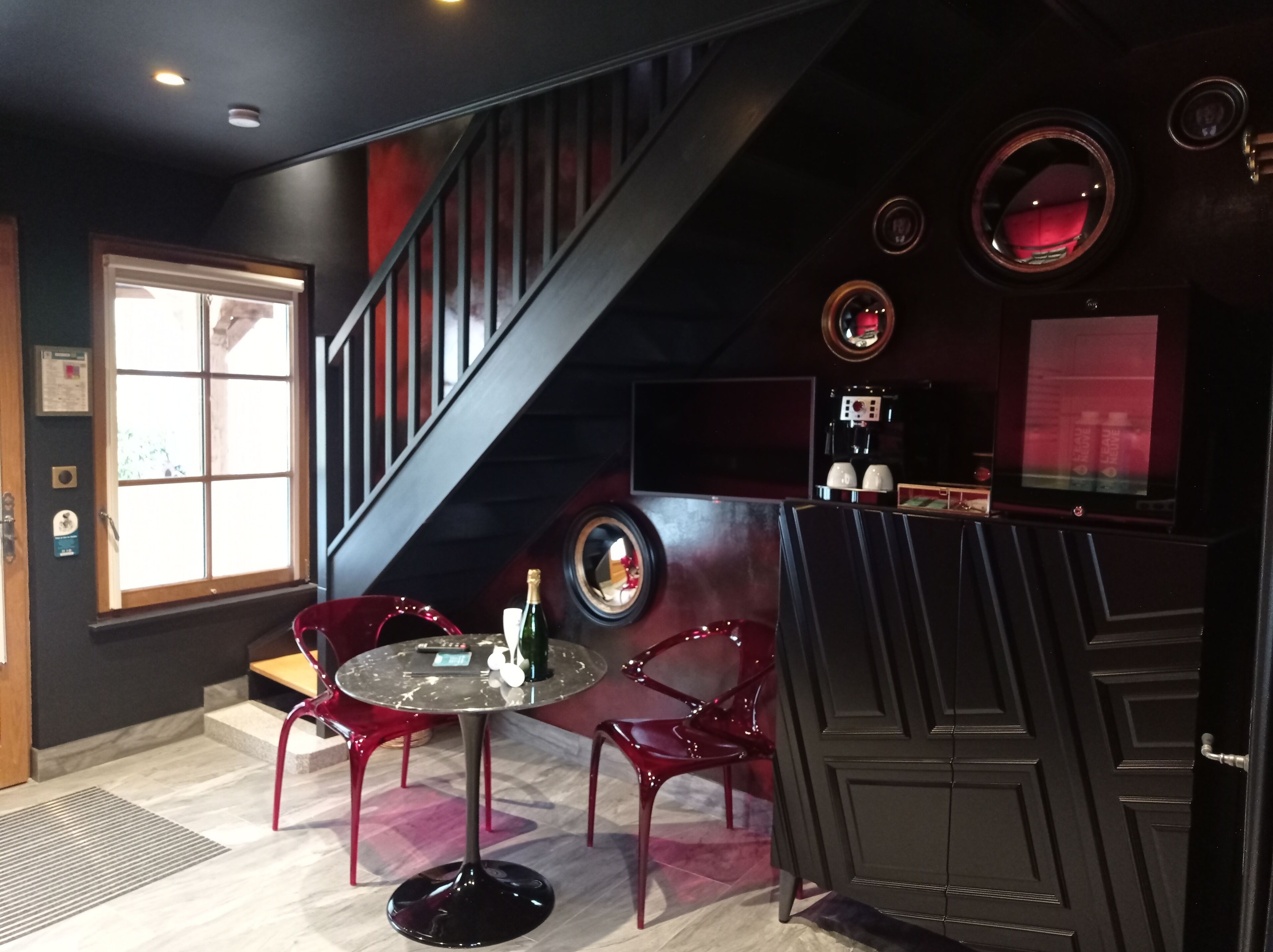 Ein modernes Interieur mit einem runden Glastisch, roten Stühlen, einer Treppe und einer Bar mit einem Fernsehbildschirm.