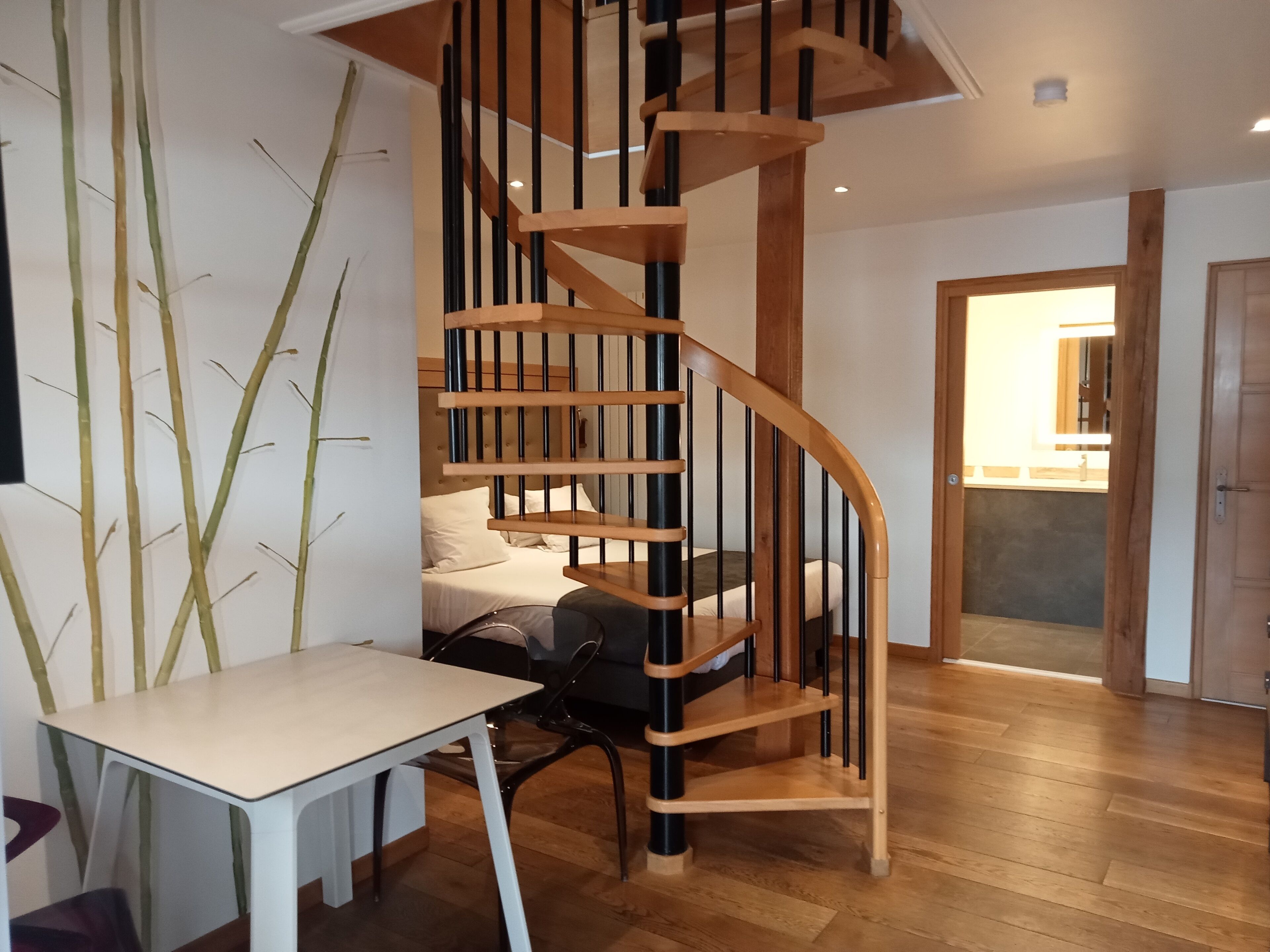 Un interior moderno con una escalera de caracol, un comedor con mesa y sillas, y un dormitorio con cama.