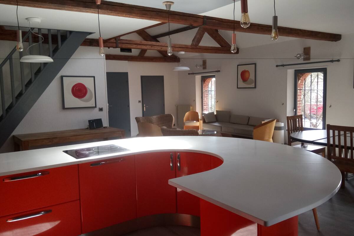 A modern kitchen with a curved red countertop, wooden beams on the ceiling, and a dining area with wooden chairs and a table.