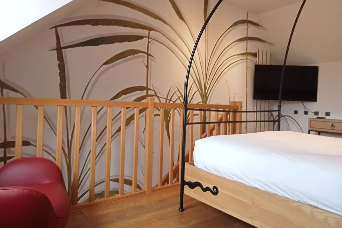 A bedroom with a sloped ceiling, a wooden bed frame, a red chair, and a wall-mounted TV.