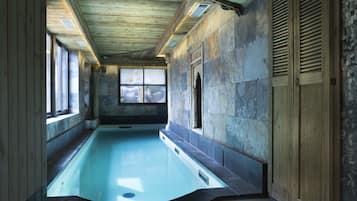 Una piscina con pareti in pietra e soffitto in legno, ampie finestre e vista sull'esterno.