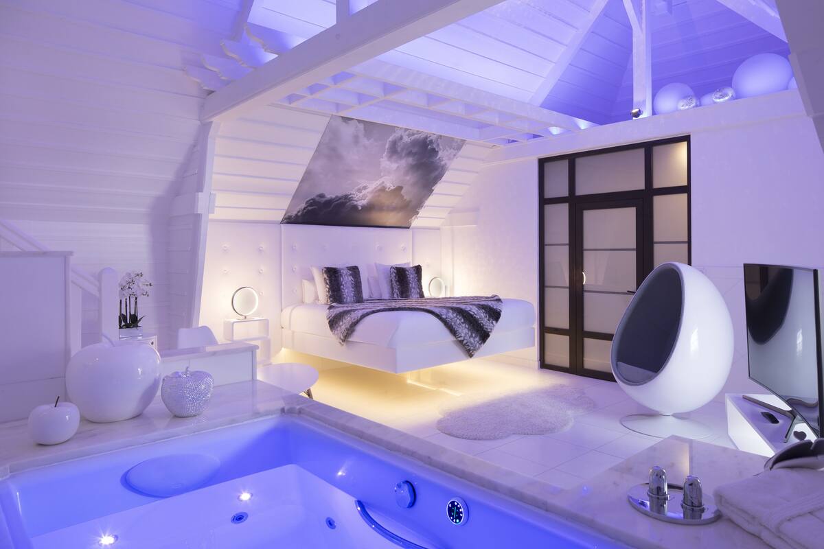 A modern bathroom with a large bathtub, a seating area with a sofa, and a large mirror.