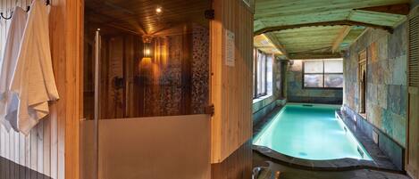 Una sauna de madera con pared de piedra y una pequeña piscina.