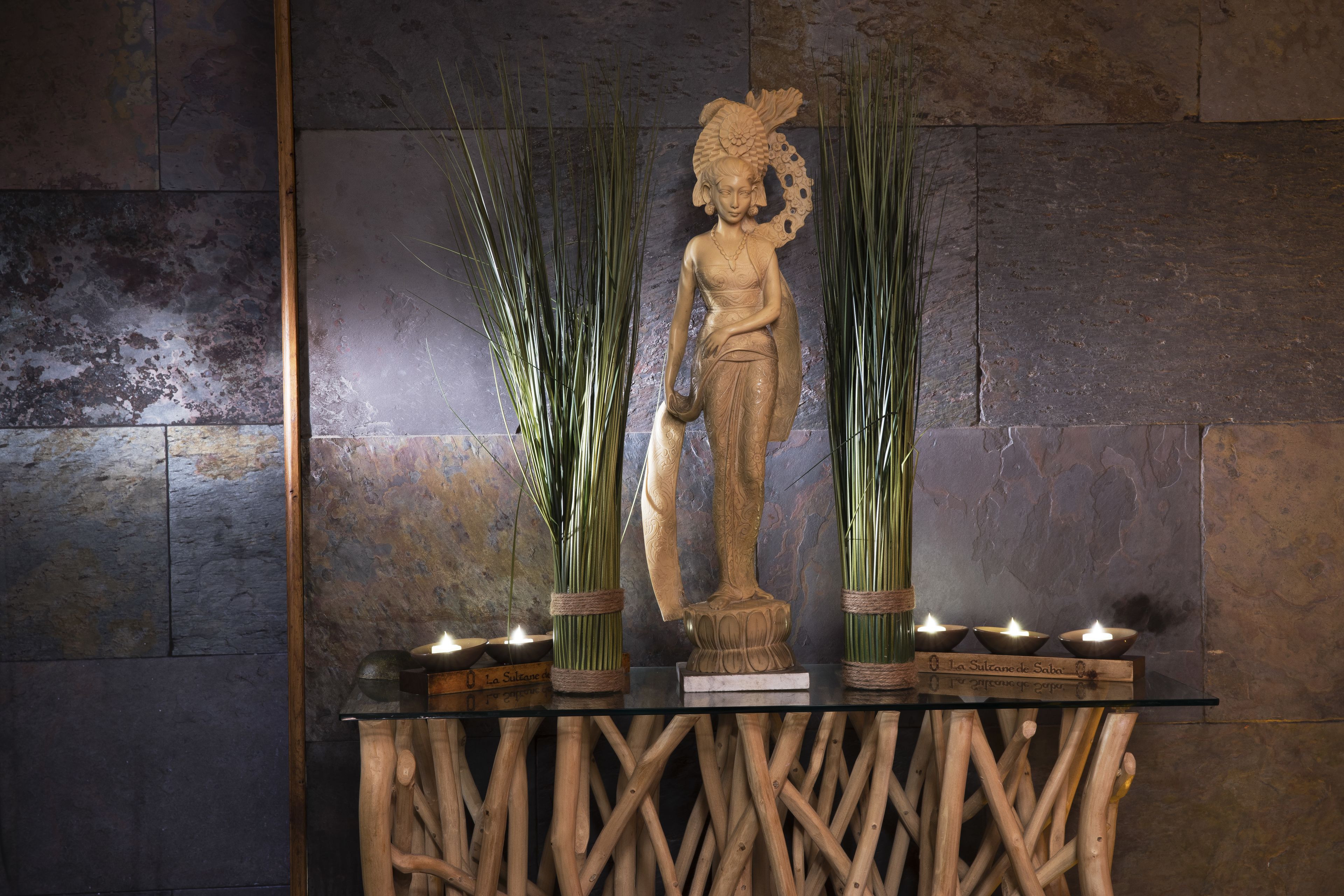 Una estatua sobre un pedestal de madera, con velas y plantas verdes.