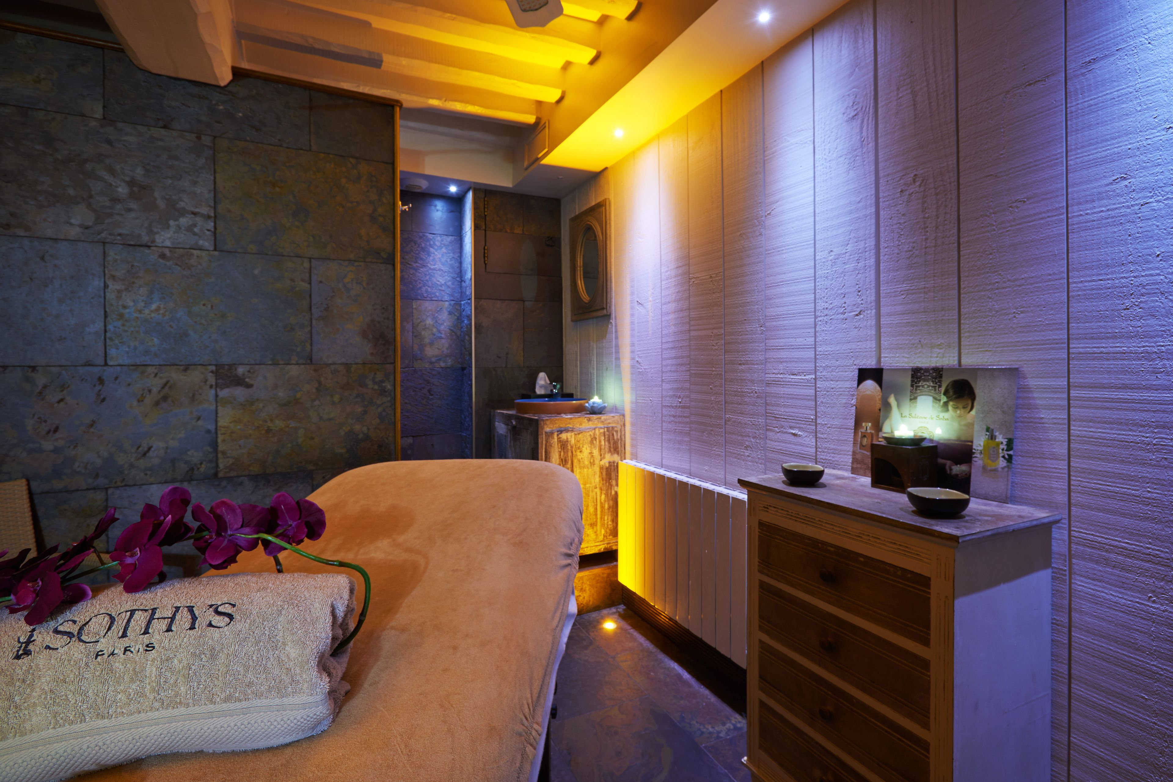 Ein Wellnessraum mit Steinwand, Holzschrank und Handtuch mit dem Schriftzug 'Sothys'.