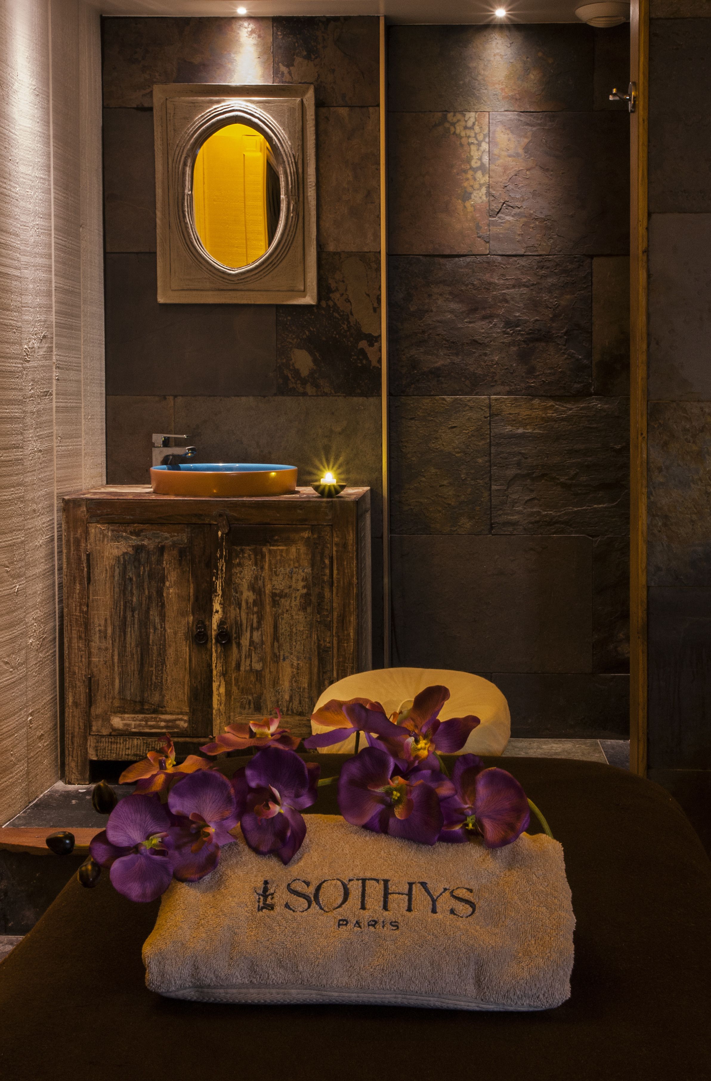 A bathroom with a wooden cabinet, a mirror, a sink, and a towel with 'SOTHYS PARIS' on it.