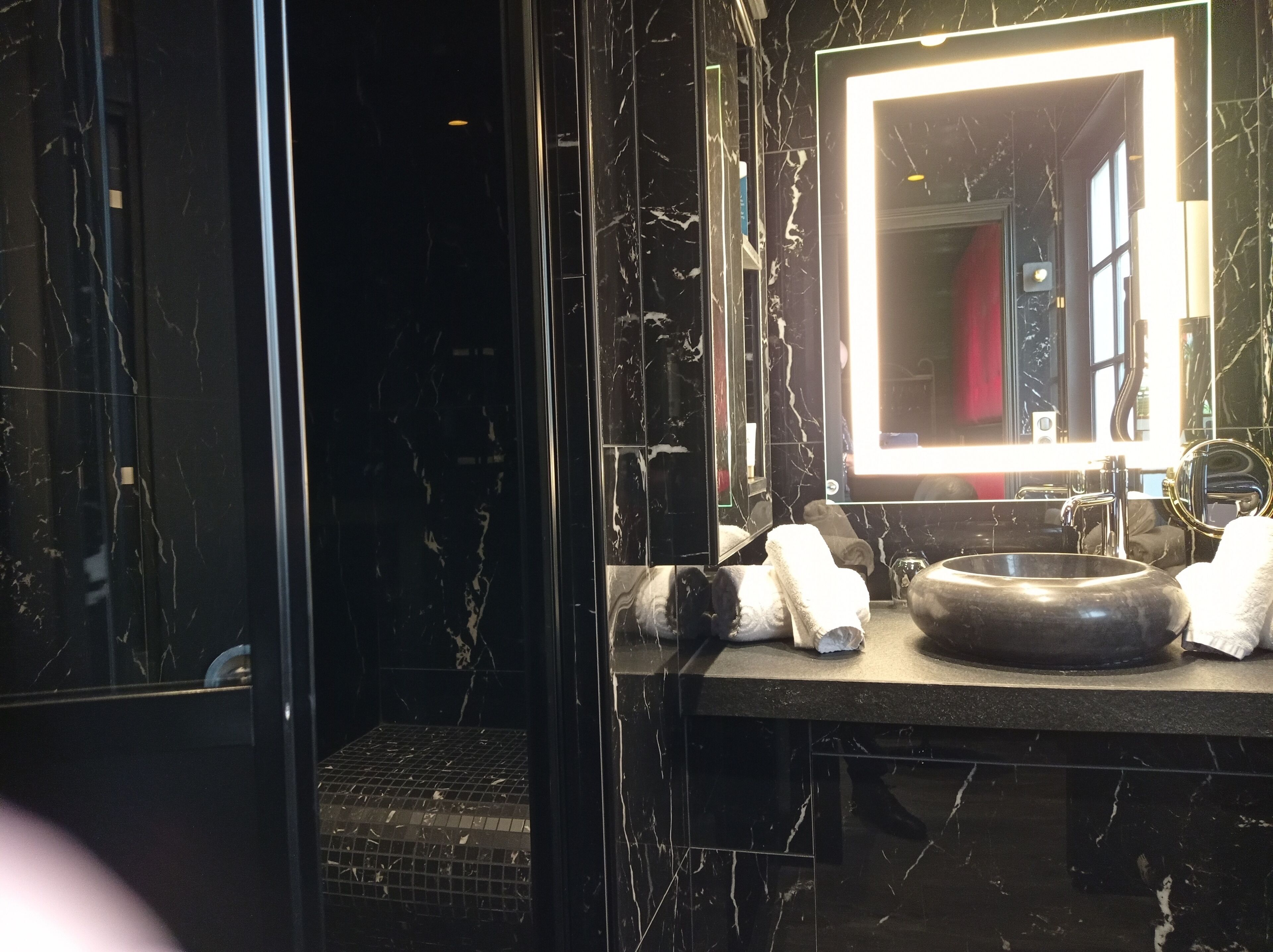 A modern bathroom with a marble vanity, a round sink, and a large mirror with a light.