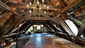 An attic room with exposed wooden beams, a brick floor, and a chandelier. - Appia Hotel Residences (Prague)
