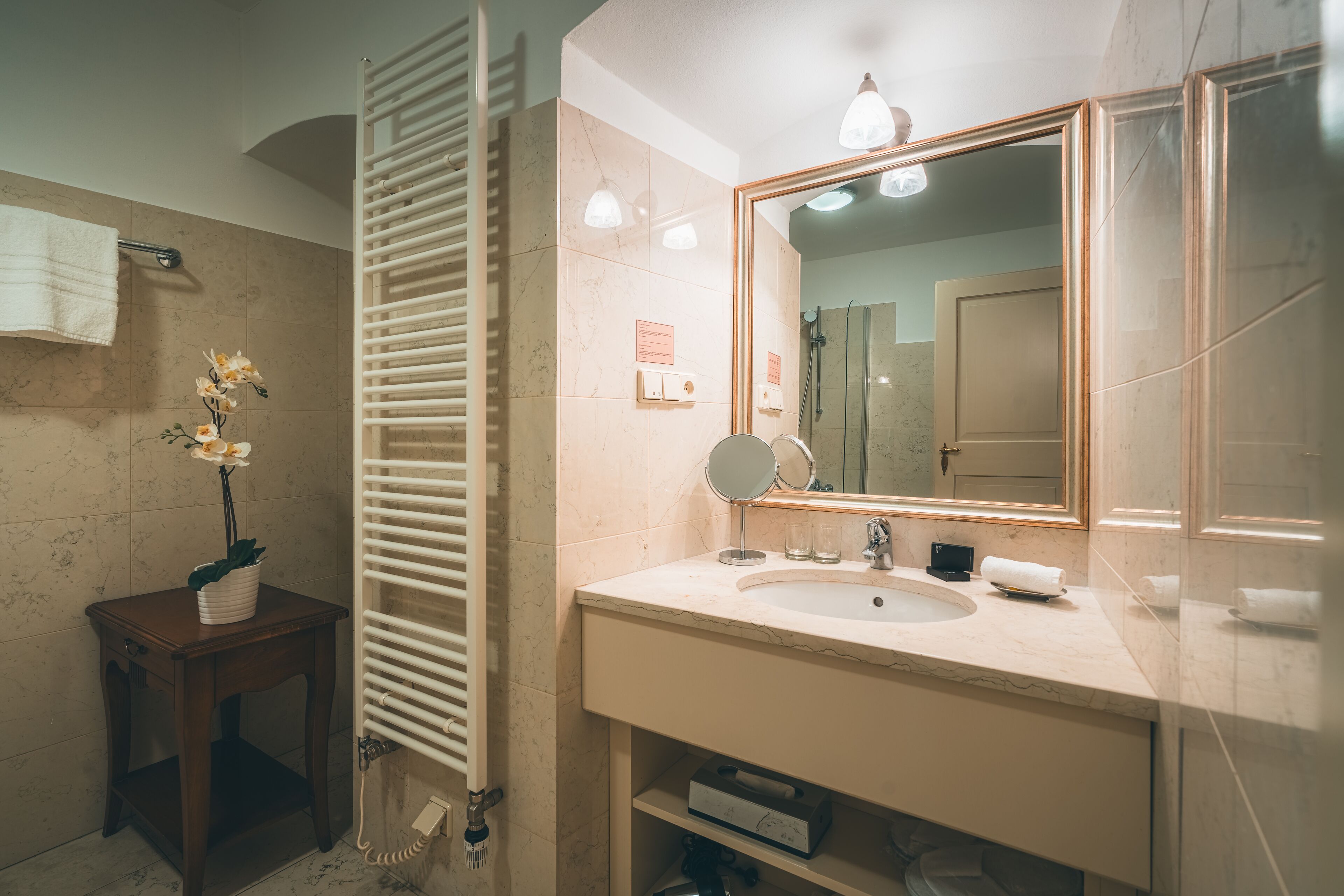 A bathroom with a marble sink, a mirror, a towel rack, and a small table with a plant.