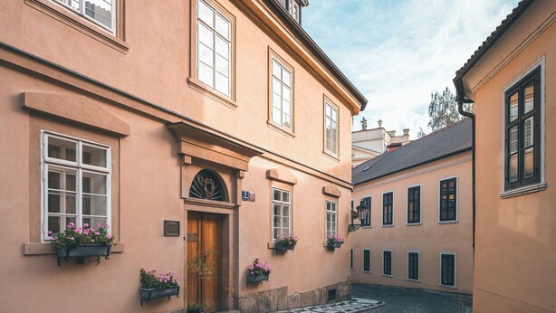 A cobblestone street with buildings featuring large windows and flower boxes. - Appia Hotel Residences (Prague)