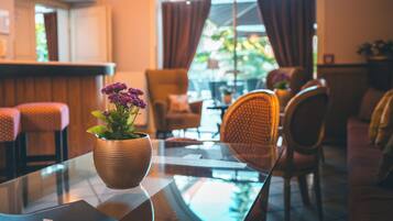 A cozy interior with a glass table, a potted plant, wicker chairs, and a view through a window with curtains.