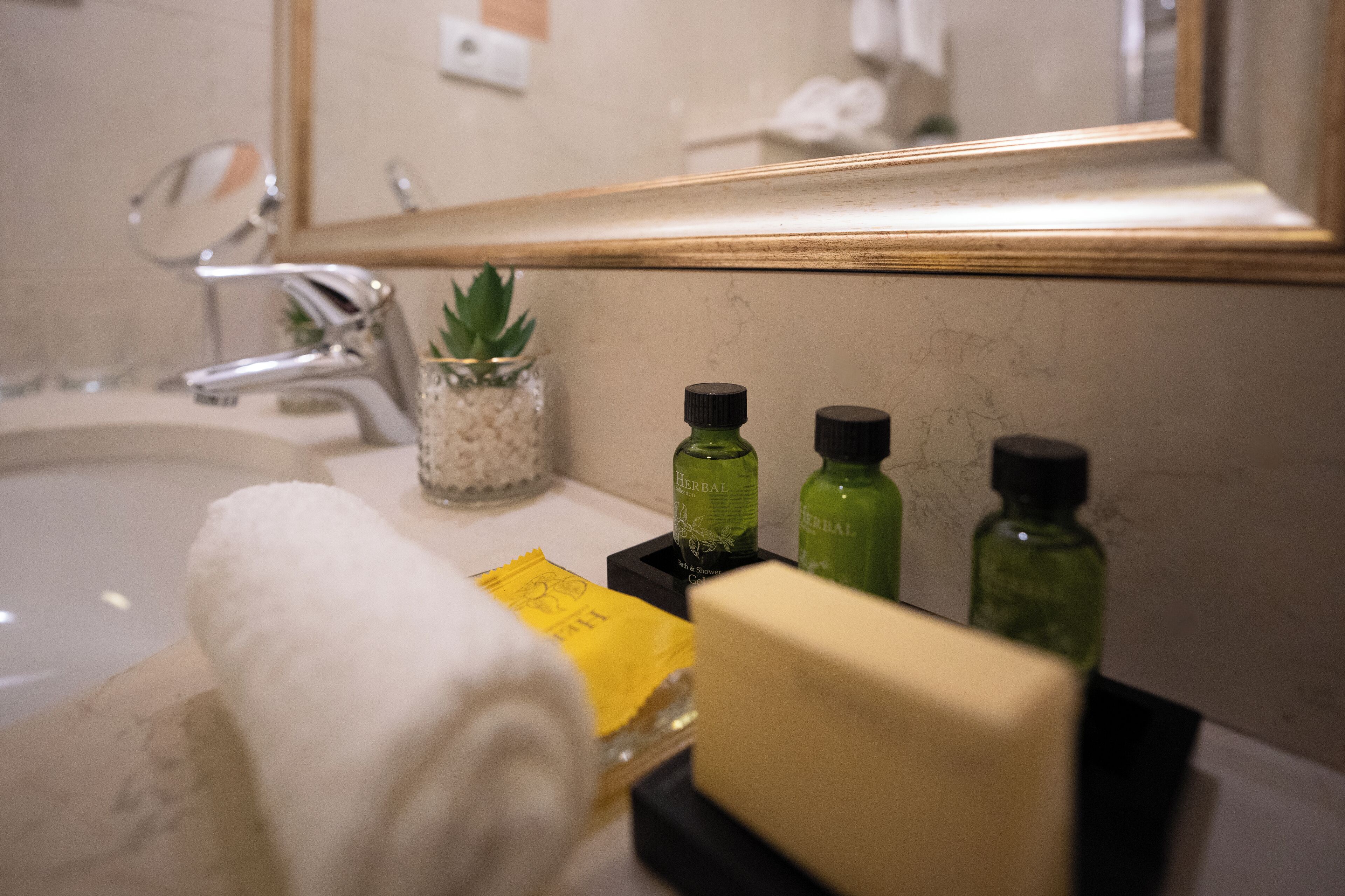 A bathroom with a sink, mirror, and toiletries including a towel, soap, and herbal bottles.