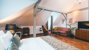 Un espacioso dormitorio tipo loft con una cama grande, una zona de estar con sofá y sillones, un televisor y una planta en maceta.
