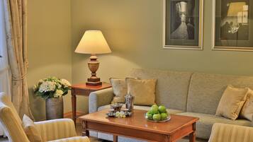 A living room with a sofa, armchairs, a coffee table with apples, a lamp, and framed pictures on the wall.