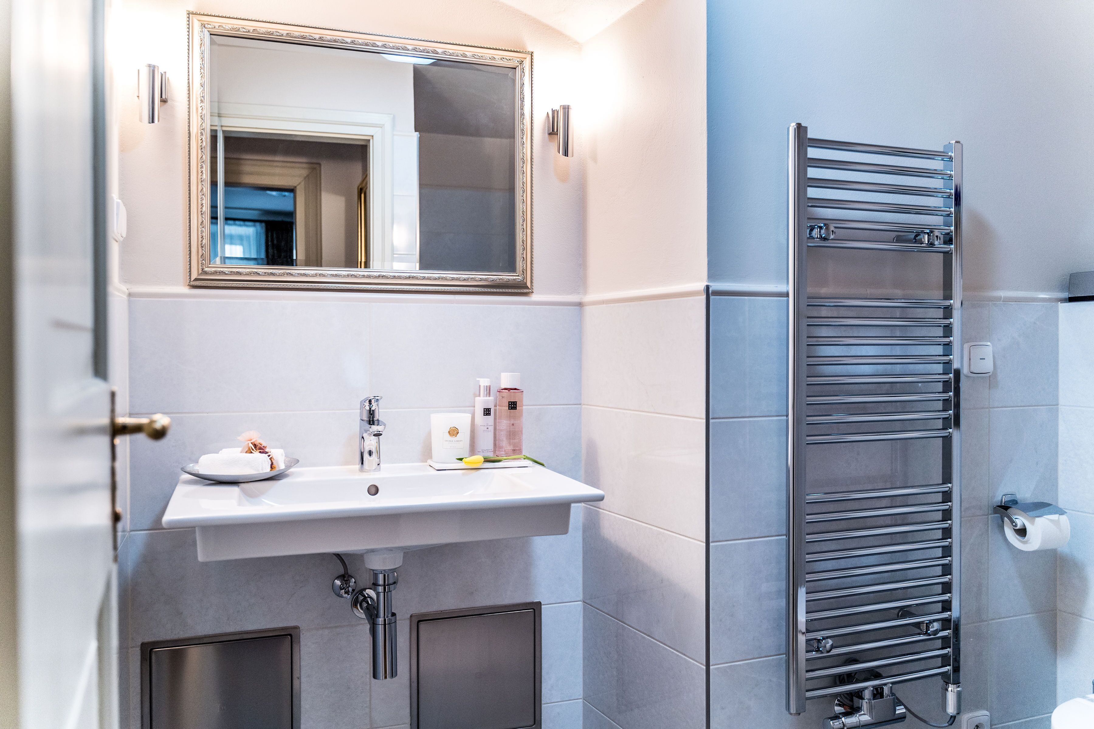 Un baño con lavamanos blanco, espejo y toallero.