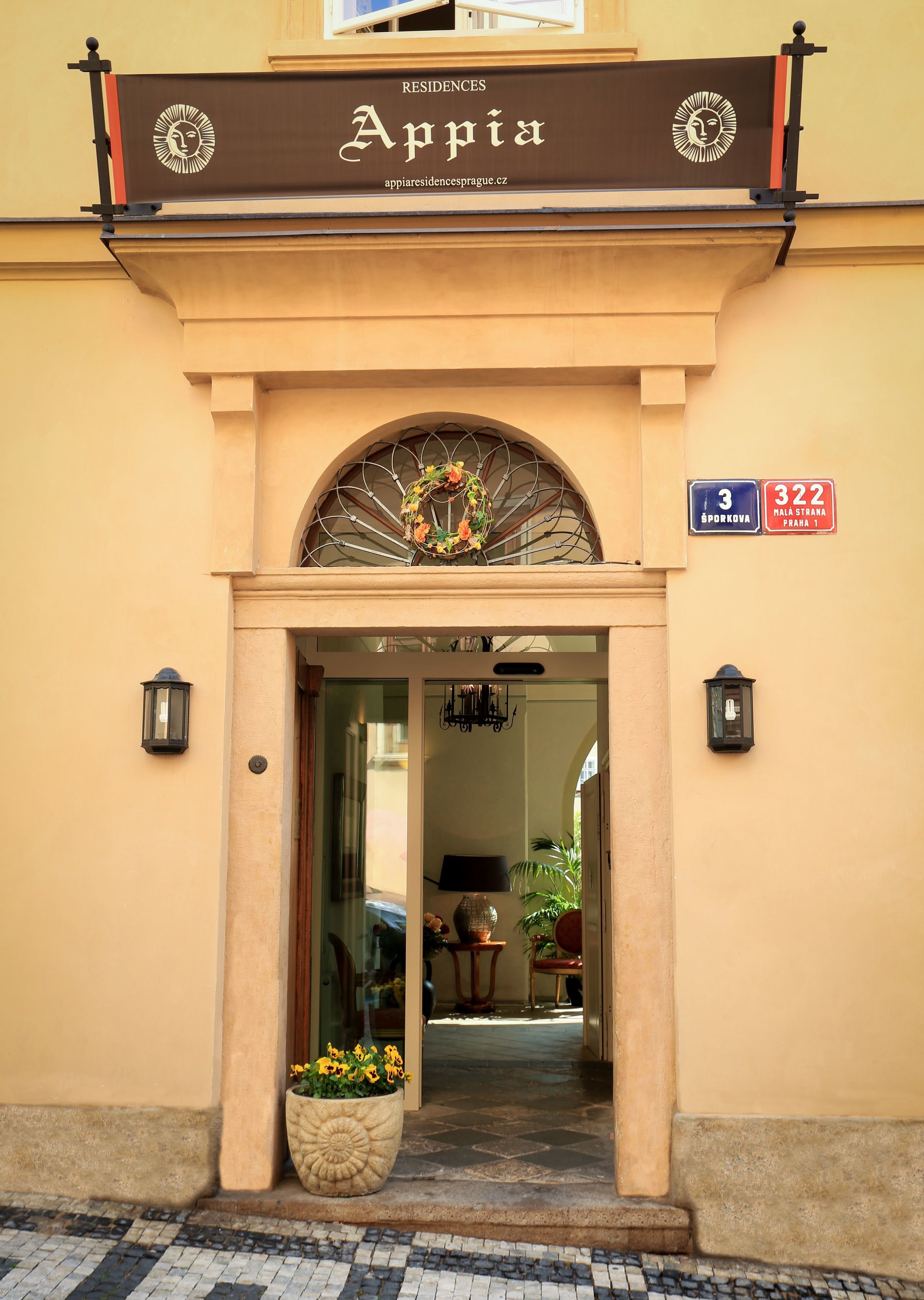 The entrance of a building with a sign reading "Appia Residences" and a street sign indicating "3 Sporkova, 322 Mala Strana Praha 1".