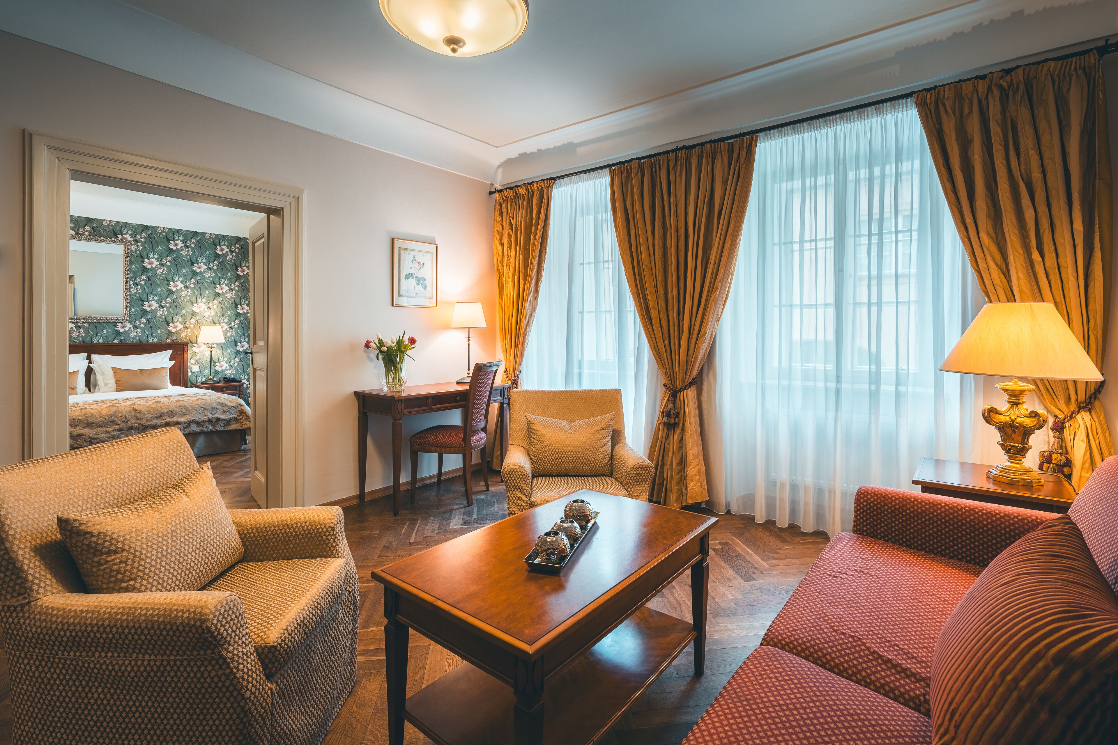 A hotel room with a wooden coffee table, two armchairs, a sofa, a bed, a desk, and a chair.