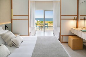 A hotel room with a bed, a desk, a chair, and a view of the sea. - Atlantica Aqua Blue (Paralimni)