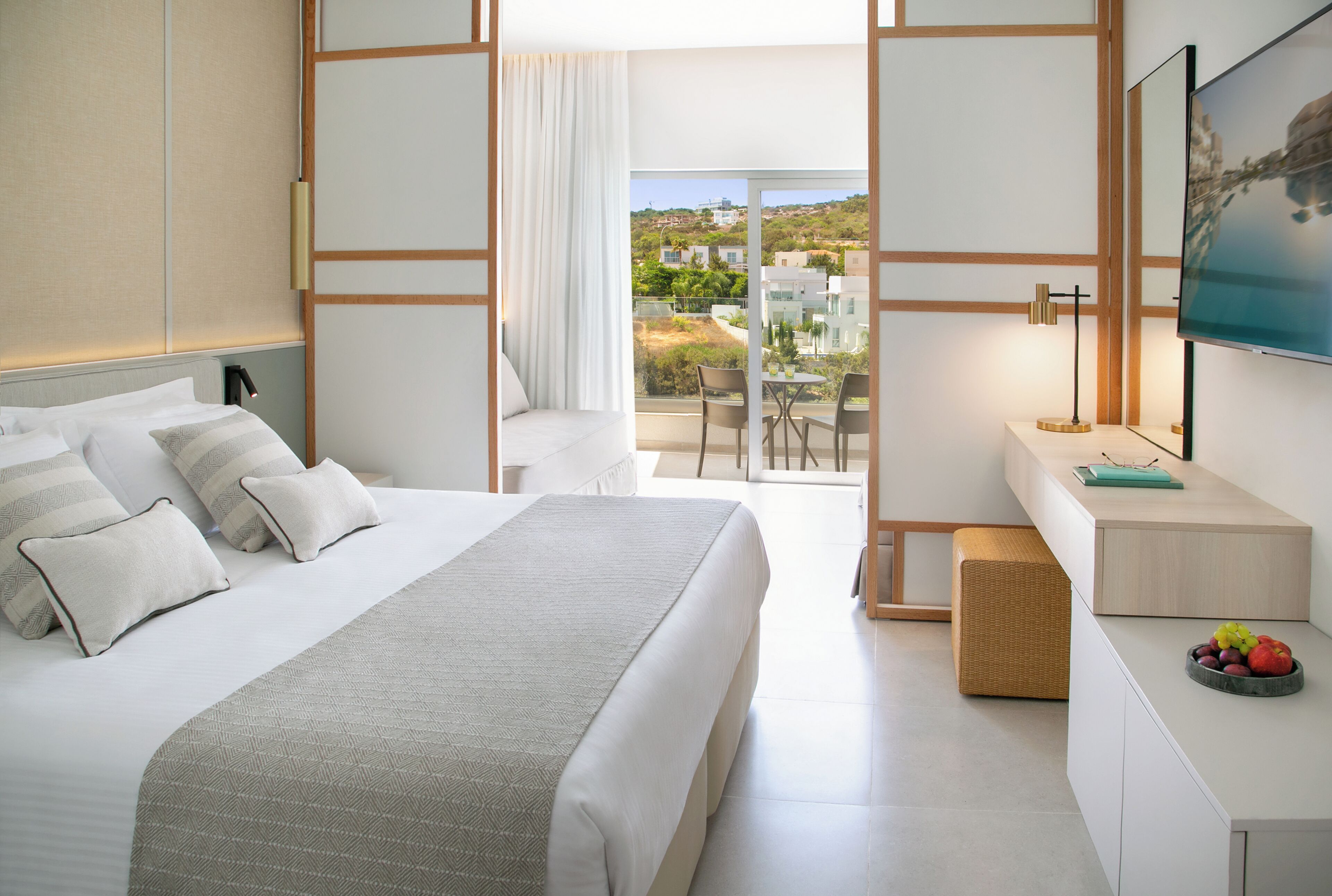 Une chambre d’hôtel moderne dotée d’un grand lit, d’un bureau avec un ordinateur, d’une télévision et d’un balcon offrant une vue sur le paysage.