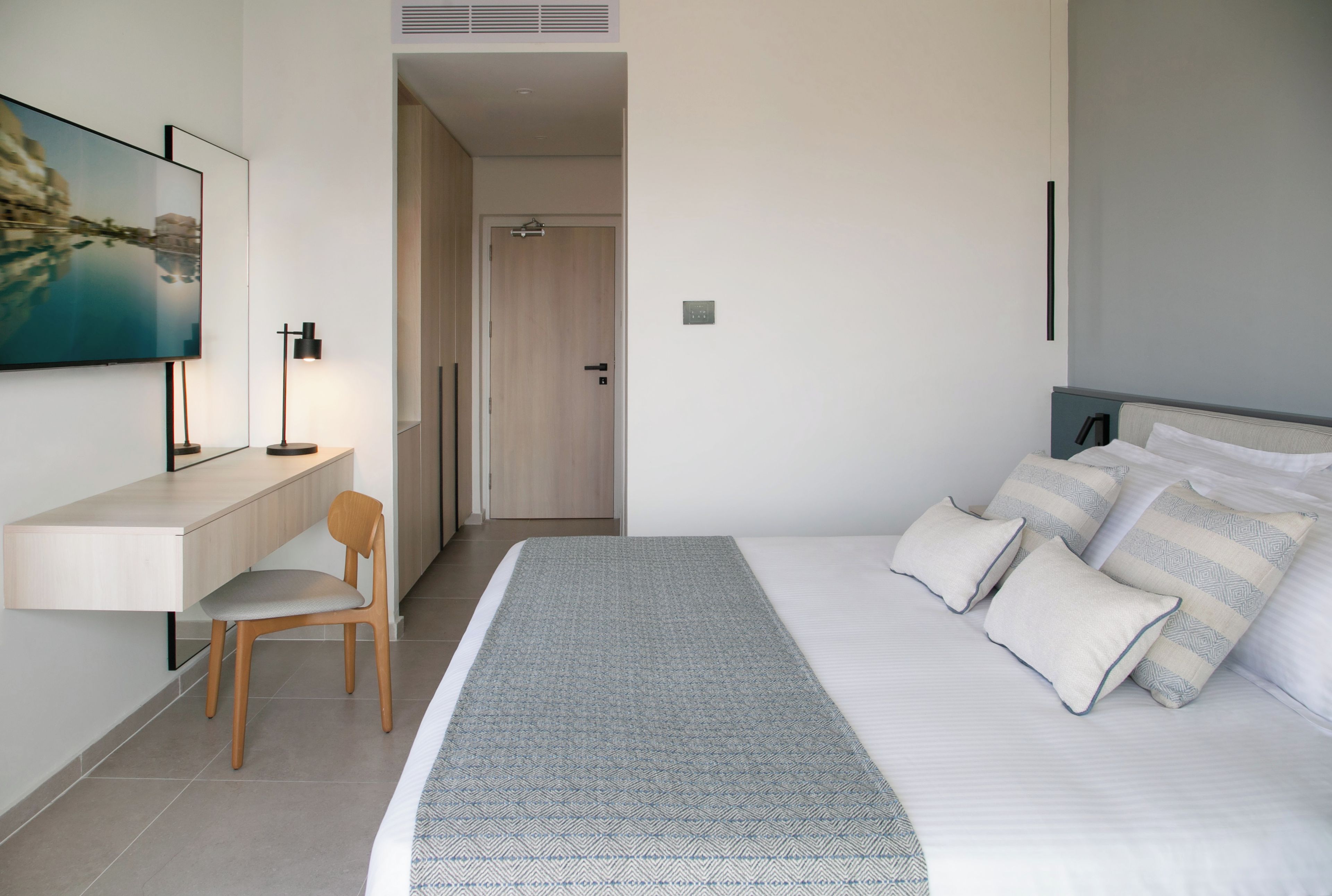 Quarto de hotel moderno com cama, escrivaninha, cadeira e um quadro na parede.