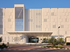 A modern hotel facade with a prominent 'SKIES' sign, a covered entrance, and a landscaped area with plants. - Atlantica Aqua Blue (Paralimni)