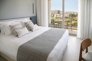 Une chambre d’hôtel avec un grand lit, une vue sur la ville depuis le balcon et un coin repas avec des chaises.